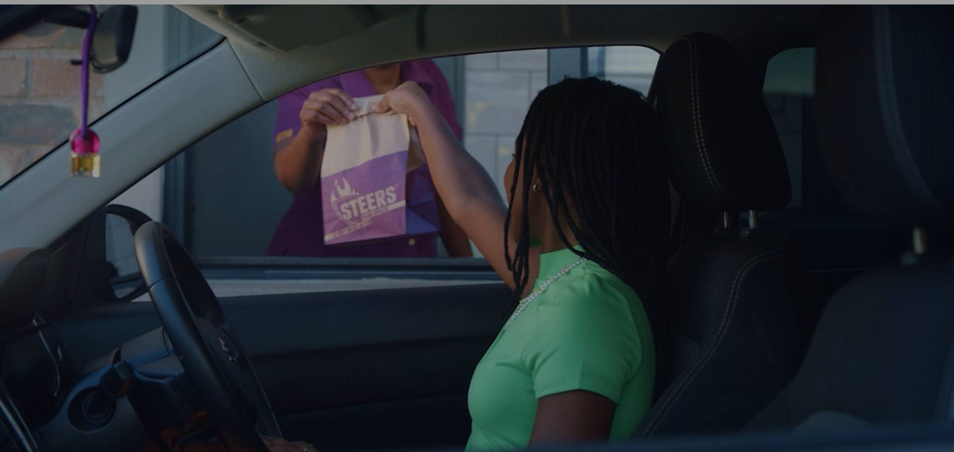 Customer inside a car receiving a fast-food takeaway bag at a drive-thru window