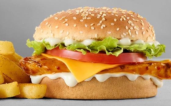 Grilled chicken chilli cheeseburger with melted cheddar cheese, lettuce, tomato slices, creamy mayonnaise sauce, sesame seed bun, and chips