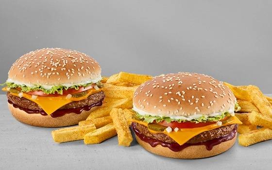 Two cheeseburgers with sliced cheese, lettuce, tomato, pickles, barbecue sauce, sesame seed buns, and chips